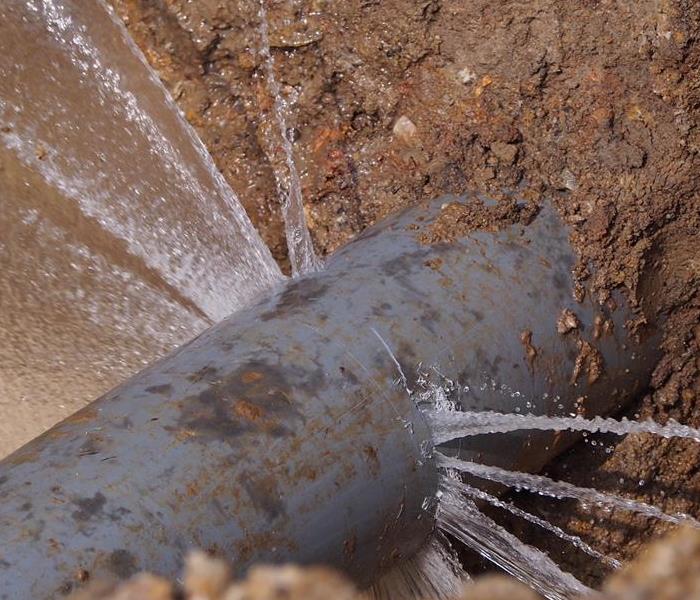 A pipe in the ground bursting out water. 