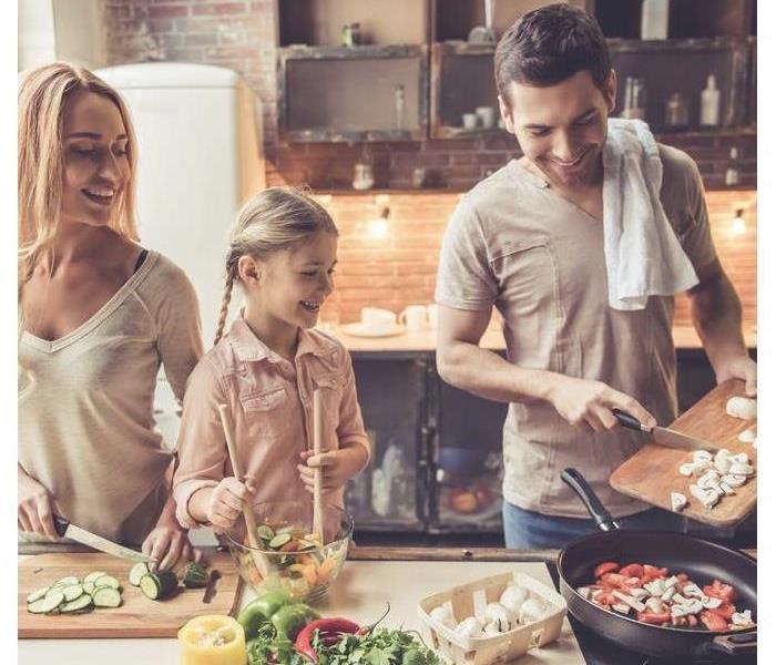 Cute little girl and her beautiful parents are smiling while cooking in kitchen at home