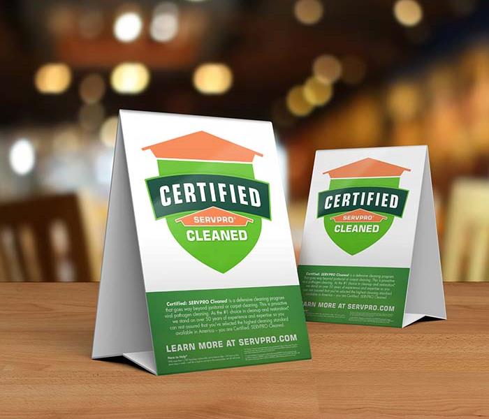 Table tent signs describing the Certified: SERVPRO Cleaned program on top of a wooden table.